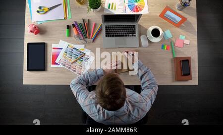 Maschio designer prendere appunti nel suo notebook per discutere con il cliente, vista dall'alto Foto Stock