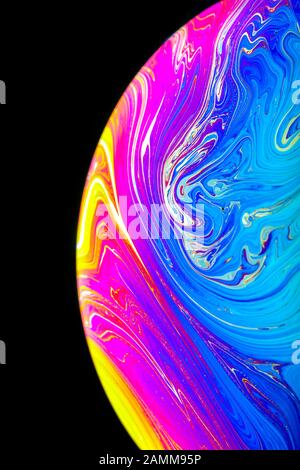 Primo piano dell'arcobaleno psichedelico di colori che si mescolano e roteano in una bolla di sapone per apparire come una galassia di fantasia o pianeta isolato uno sfondo nero Foto Stock