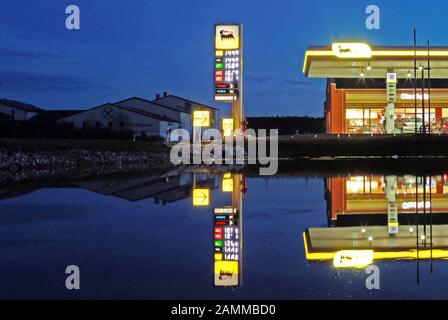 La stazione di servizio Agip notturna si riflette sulla superficie dell'acqua di un corso d'acqua alla periferia di Moorenweis. [traduzione automatizzata] Foto Stock