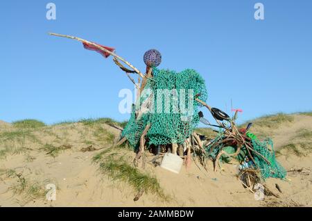 Scultura realizzata da rifiuti in plastica e spazzatura detriti sulla spiaggia pronti per essere raccolti Foto Stock