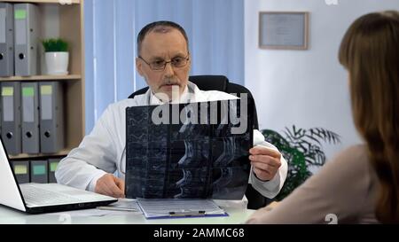 Chirurgo attento che guarda il collo raggi X, lavorando sulla diagnosi, appuntamento Foto Stock