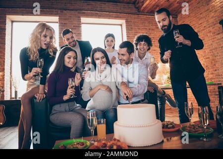 Foto di gruppo migliori amici venuti a visitare una coppia sposata in attesa bambino nato disponendo sorpresa baby party porterà grande torta andando a mangiare usura convenzionale Foto Stock