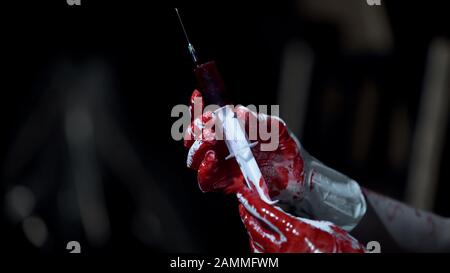 Persona insana in guanti di lattice che contengono siringa con sangue, crimine orribile, spaventoso Foto Stock