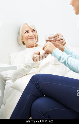 Senior a letto prende medicina con acqua in una casa di cura Foto Stock