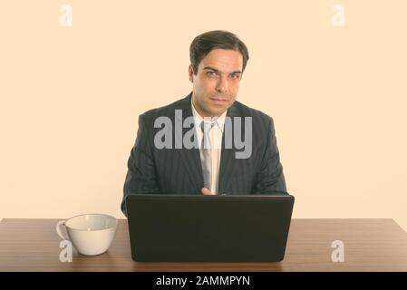 Uomo d'affari persiano seduto con un laptop e una tazza di caffè su un tavolo di legno Foto Stock