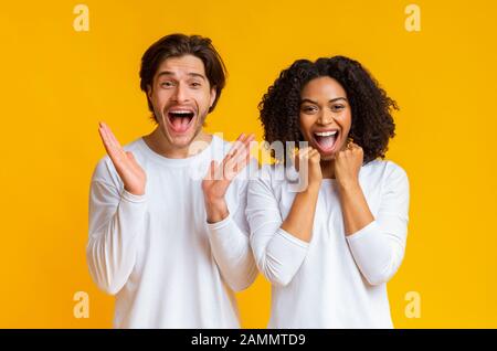 La coppia Interracial gioisce emozionalmente il successo, alzando le mani ed esclamando con eccitamento Foto Stock