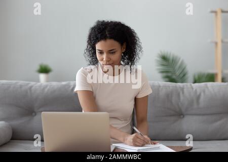 La donna africana guarda al computer notando di lavorare in remoto Foto Stock