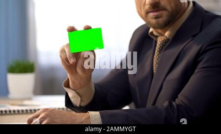 Uomo d'affari seduto alla scrivania in ufficio, mostrando carta verde, servizi bancari Foto Stock