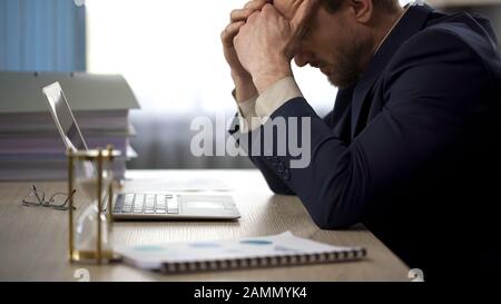 Lavoratore aziendale seduto alla scrivania, rubbing templi, stanchezza, lavoro straordinario Foto Stock