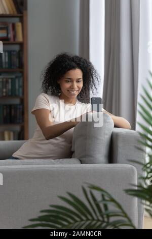 Donna africana seduta sul divano utilizzando smartphone divertirsi online Foto Stock