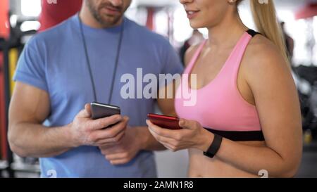 Fit lady che mostra l'applicazione che tiene traccia dei suoi risultati al personal trainer in palestra Foto Stock