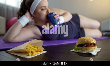 Ragazza pigra obesa in soda bevuta sportswear invece di allenarsi su stuoia yoga Foto Stock
