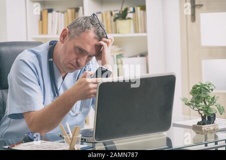 Oberati di lavoro medico seduto nel suo ufficio Foto Stock