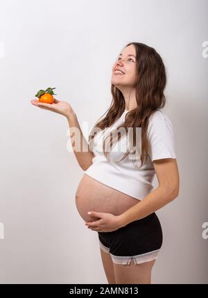 Immagine della donna incinta di toccare la sua grande pancia e tenendo premuto mela gialla in mano su sfondo bianco. Foto Stock