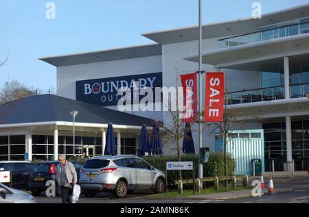 Woman Shopper By Parched Cars Outside Boundary Mills Retail Shopping Outlet A Colne, Pendle, Lancashire, Inghilterra, Regno Unito. Foto Stock