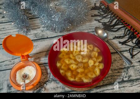 Ciotola rossa piena di deliziosi tortellini in brodo, piatto tipico della cucina italiana per proteggersi dal freddo Foto Stock