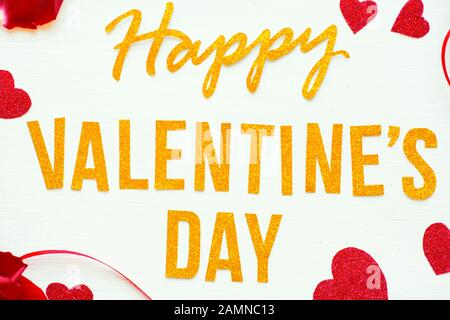 Oro testo Happy Valentines giorno biglietto di auguri con petali di rosa rossa e cuori su sfondo bianco di legno. Concetto romantico e amore Foto Stock