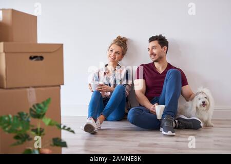 Coppia sorridente con tazze da caffè che si rilassano nella loro nuova casa Foto Stock