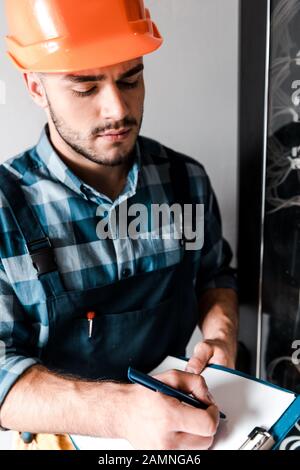 bell'uomo di lavoro che tiene gli appunti mentre scrive vicino a fili e cavi Foto Stock