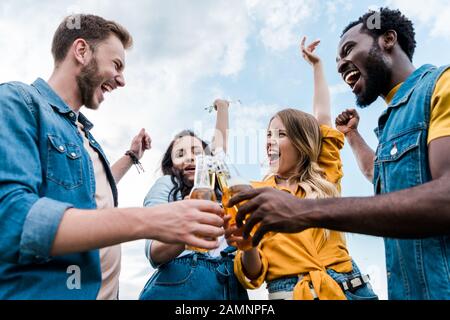 vista a basso angolo di felice multiculturale uomini e donne bottiglie in clinking con birra Foto Stock