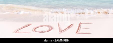 Amore scritto sulla sabbia bianca di una spiaggia idilliaca, panoramica San Valentino banner Foto Stock
