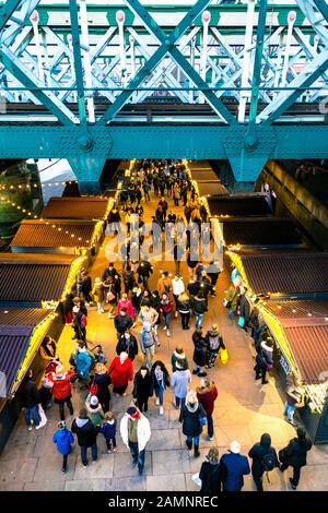 Persone e bancarelle sotto l'Hungerford Bridge presso il festoso Southbank Center Winter Market, Londra, Regno Unito Foto Stock