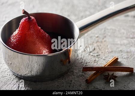 deliziosa pera nel vino in padella vicino alla cannella e anice su superficie di cemento grigio Foto Stock