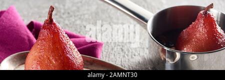 deliziosa pera al vino su piastra d'argento e in pentola su cemento grigio con tovagliolo rosa, colpo panoramico Foto Stock