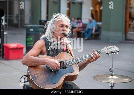 Oslo, Norvegia-1 agosto 2013: Un musicista di strada si esibisce sulla strada principale di Karl Johans gate. Un uomo anziano con lunghi capelli bianchi, guadagna soldi su Th Foto Stock