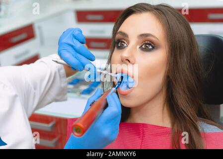 Restauro odontoiatrico in odontoiatria con lampada in fotopolimero. La ragazza all'appuntamento del dentista. Procedure dentali Foto Stock