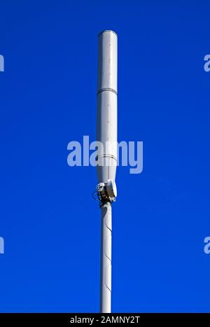 Un palo del telefono mobile in una città nel Regno Unito visto contro un cielo blu chiaro Foto Stock