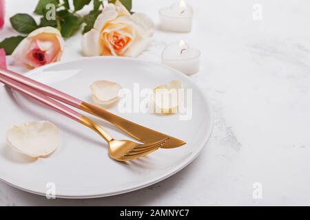 Piastra con la forchetta e il coltello e petali di rosa e rose un tavolo bianco di close-up.
