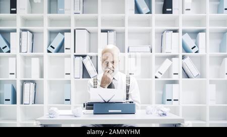 Uomo d'affari o giornalista senior che lavora in ufficio, è seduto alla scrivania e utilizza una macchina da scrivere Foto Stock