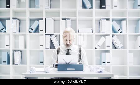 Uomo d'affari o giornalista senior che lavora in ufficio, è seduto alla scrivania e utilizza una macchina da scrivere Foto Stock