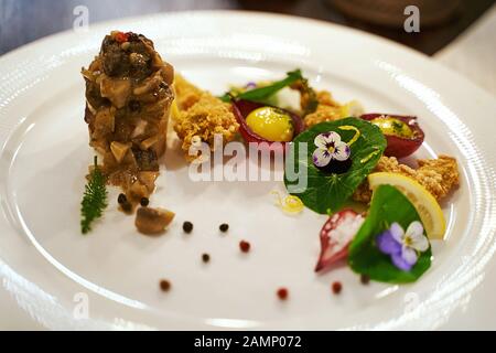 Cucina alta o cucina alta concetto di cibo. Cosce di rana e midollo osseo servite con sugo e fiori crudi viola commestibili. Squisito pasto esclusivo. Foto Stock