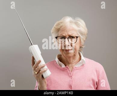 Donna anziana frustrata che usa un vecchio telefono cordless, sta guardando la macchina fotografica delusa Foto Stock