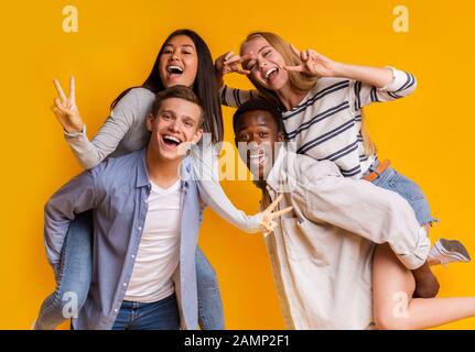 Due coppie teen internazionali che si divertono su sfondo giallo Foto Stock
