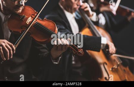 Orchestra d'archi sinfonica professionale che si esibisce sul palco e suona un concerto di musica classica, violinista in primo piano Foto Stock