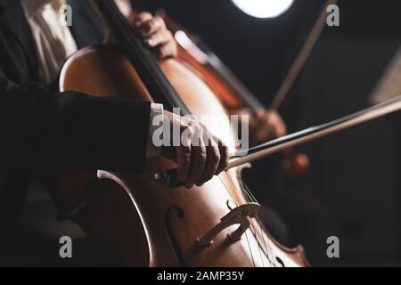 Orchestra sinfonica che si esibisce sul palco e suona un concerto di musica classica, violoncellista in primo piano, si avvicina Foto Stock