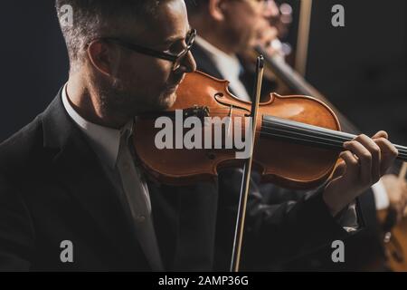 Orchestra d'archi sinfonica professionale che si esibisce sul palco e suona un concerto di musica classica, violinista in primo piano Foto Stock