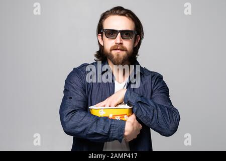 Giovane bell'uomo con barba su sfondo bianco isolato con occhiali 3d e tenendo un grande secchio di pop-corns Foto Stock