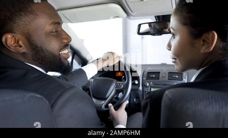 Due colleghi multietnici che si flirtare, discutere di affari in auto, avendo affare Foto Stock