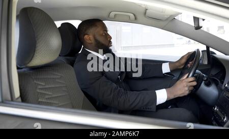 Occupato afro-americano uomo in vestito costoso guidare a riunione di affari in auto Foto Stock