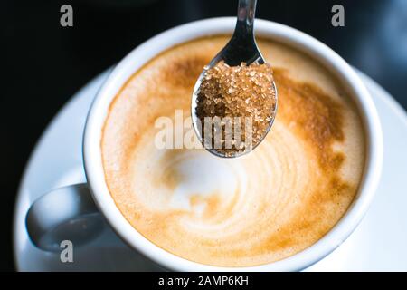versare lo zucchero di canna nel caffè Foto Stock