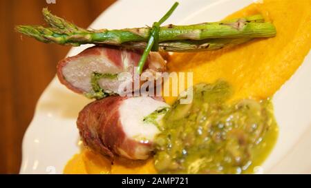 Un ristorante piatto principale di pollo avvolto nel prosciutto di Parma è servito con asparagi, funghi e dolce purea di patate. Foto Stock