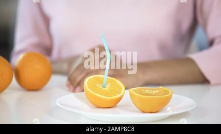 Metà arancione fresco con paglia di fronte alla giovane donna sul piatto, stile di vita sano Foto Stock