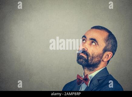 Headshot confuso uomo che pensa guardando verso il lato interessato isolato su sfondo grigio con spazio di copia sopra la testa per il tuo testo o il tuo design. Umano Foto Stock