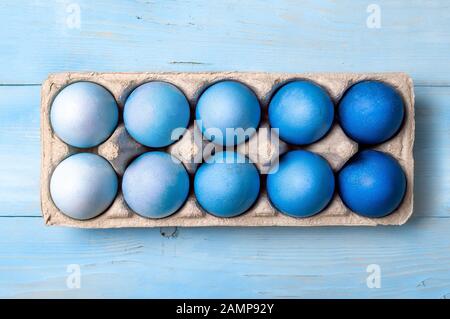 Concetto di Pasqua. Uova Ombre in colori blu in cartone imballaggio su sfondo di legno blu. Vista dall'alto verso il basso o piatto. Colori blu classici a Pasqua 2020 Foto Stock