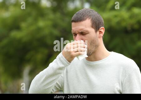 L'uomo malato soffia usando un tessuto di carta che sta in piedi in un parco Foto Stock