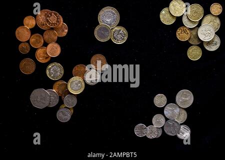 Pile di vari tipi di monete di diverse forme e da vari paesi organizzati per tipo di metallo su sfondo nero Foto Stock